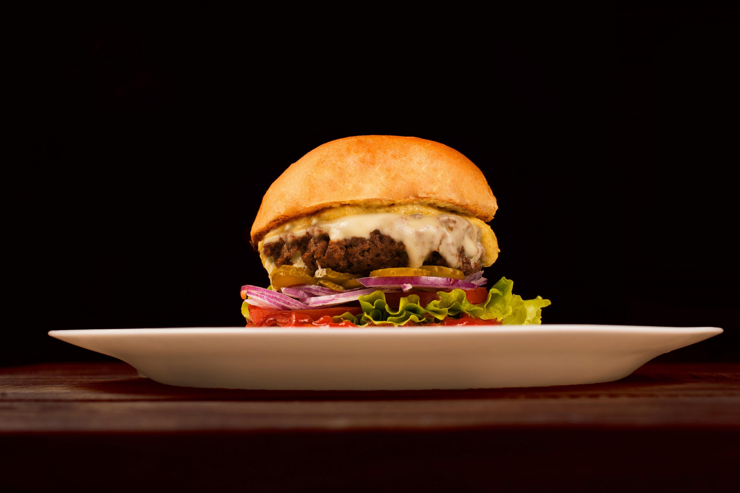 Mouth-watering cheeseburger with fresh veggies and melted cheese on a white plate.