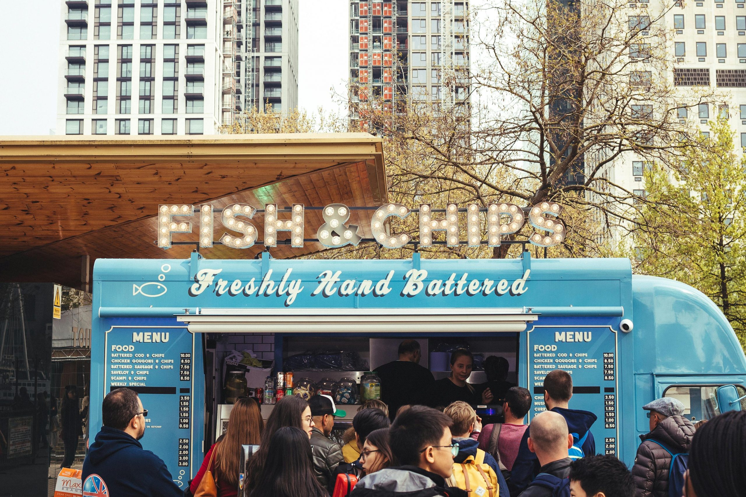 Services Crowd enjoying fish and chips at a lively food truck with urban buildings in the background.