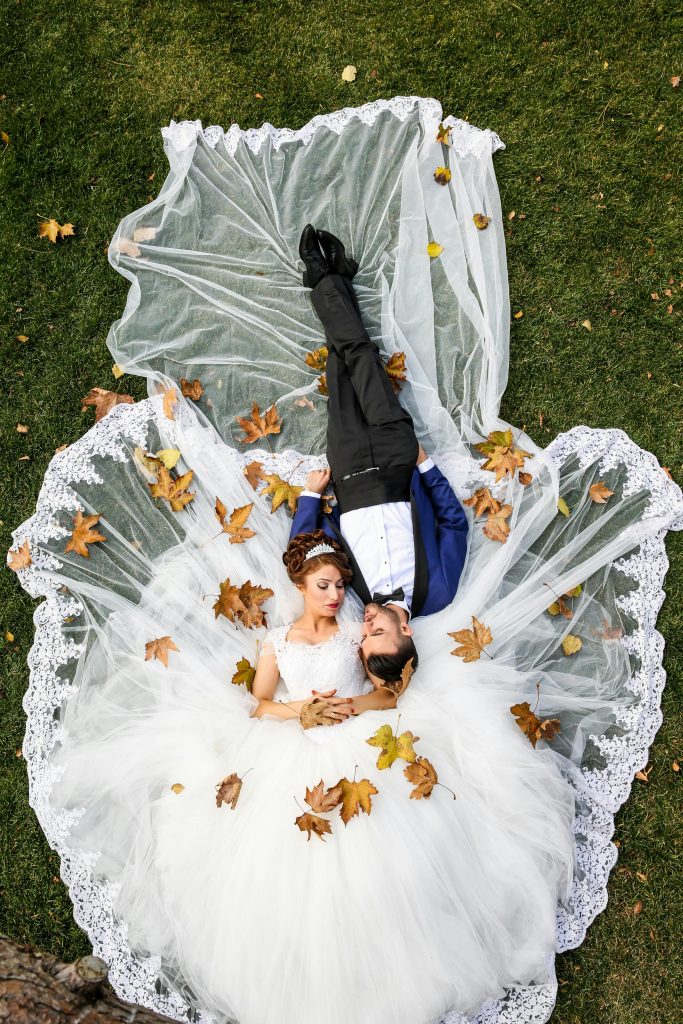 Bride and groom lying together on a lawn surrounded by autumn leaves, captured from above. Location food truck mariage