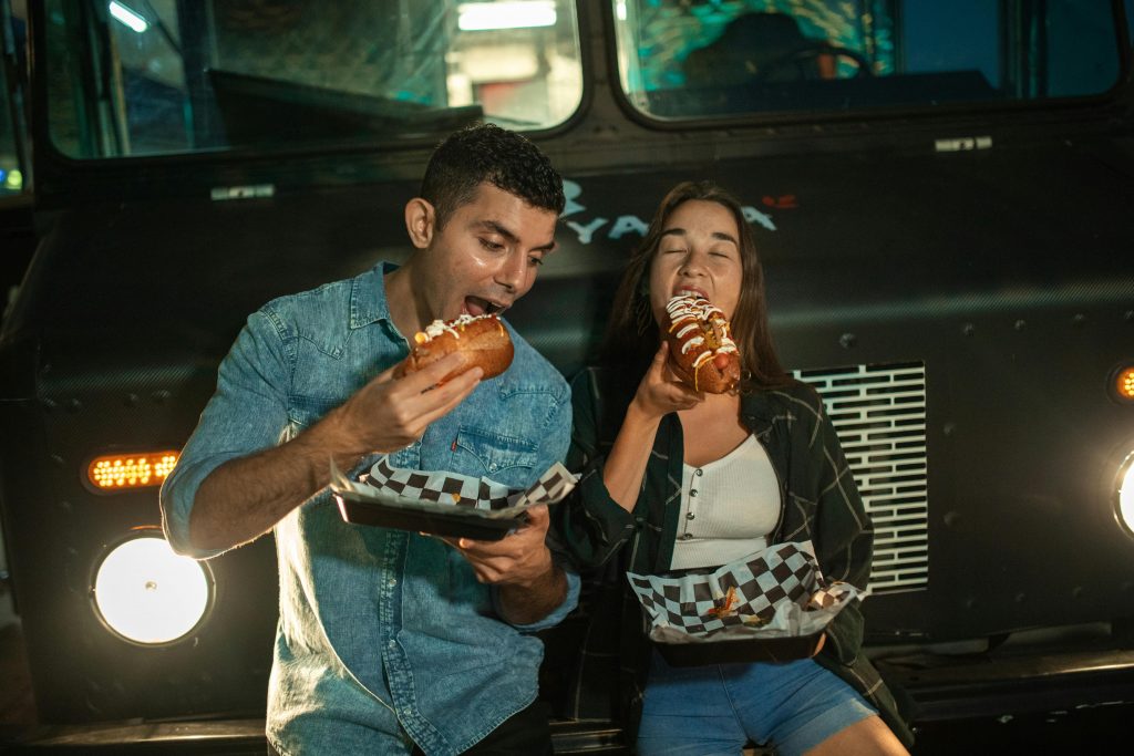 Happy couple eating hot dogs at a food truck, enjoying a casual night out.