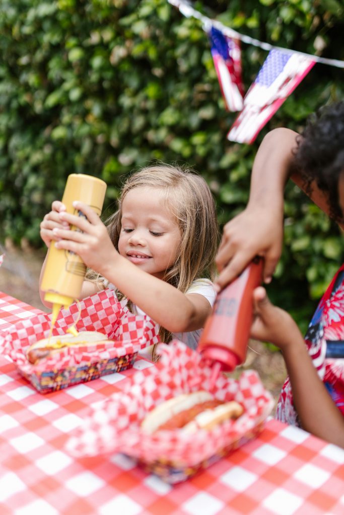 Kids adding condiments to hot dogs during a fun outdoor family picnic. Food truck hot dog