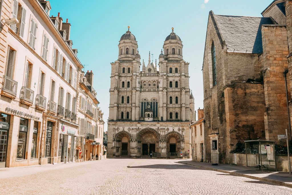 Beautiful basilica and charming street in Dijon, France under a bright blue sky.