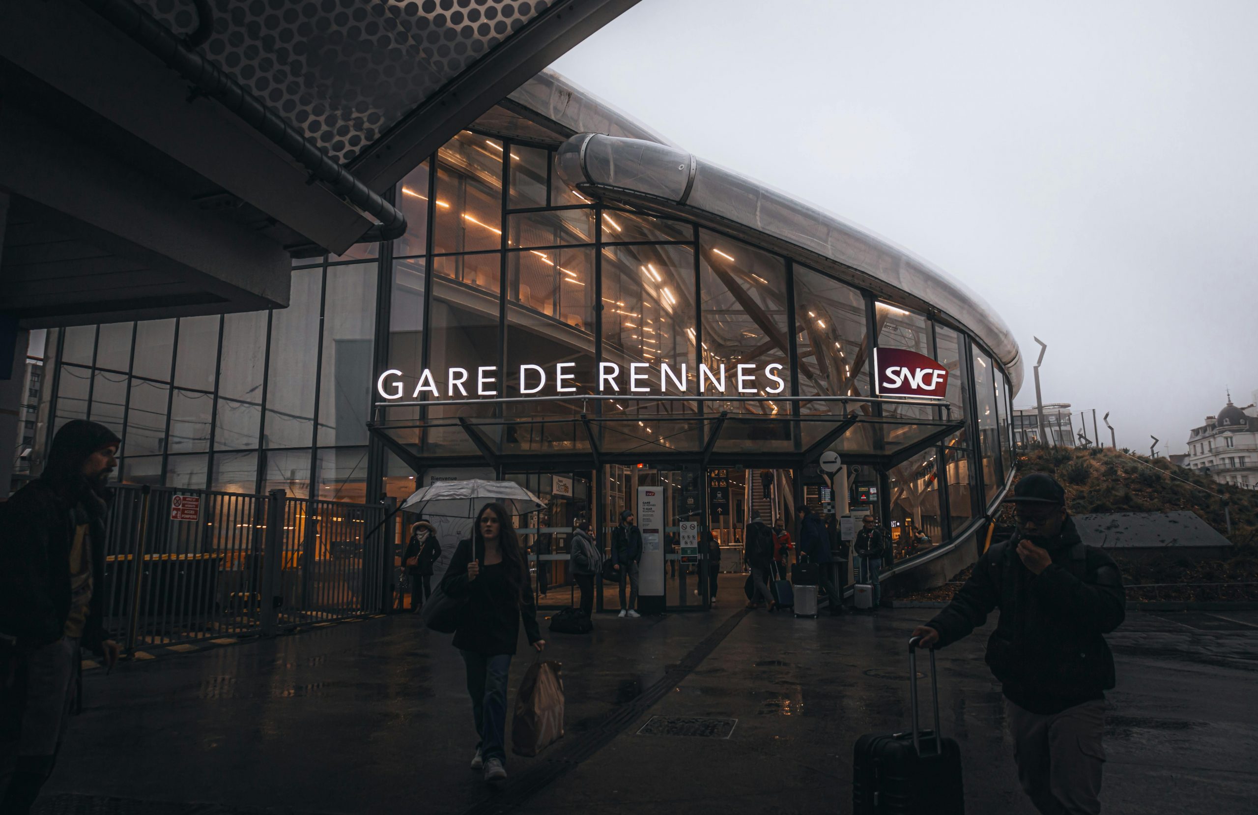People entering Gare de Rennes on a misty day in France, showcasing urban life.